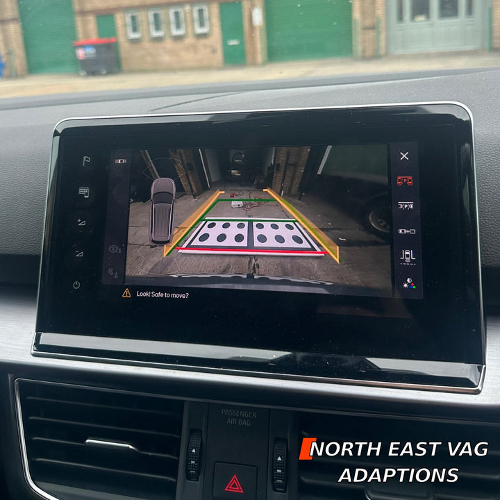 Dashboard touchscreen showing a rear camera view of a workshop floor with a black-dotted target board and guide lines