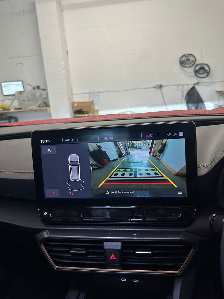 Touchscreen showing a rear camera view of a workshop with a black-dotted target board, guide lines and a top-down car icon