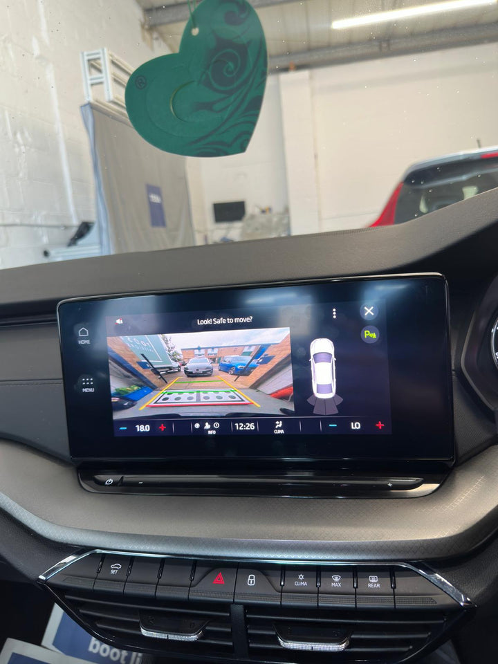 Dashboard touchscreen showing a rear camera view of a car park with a dotted target board and a top-down car icon