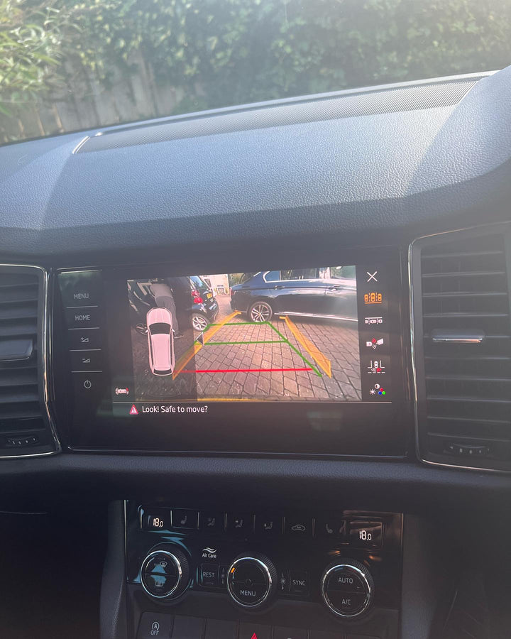 Dashboard touchscreen showing a rear camera view of a block-paved drive with yellow, green and red guide lines