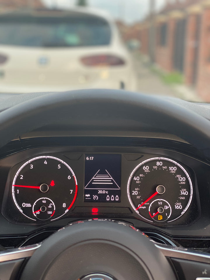 Instrument cluster behind the steering wheel, centre display showing a road graphic and 20.0°C, blurred car ahead